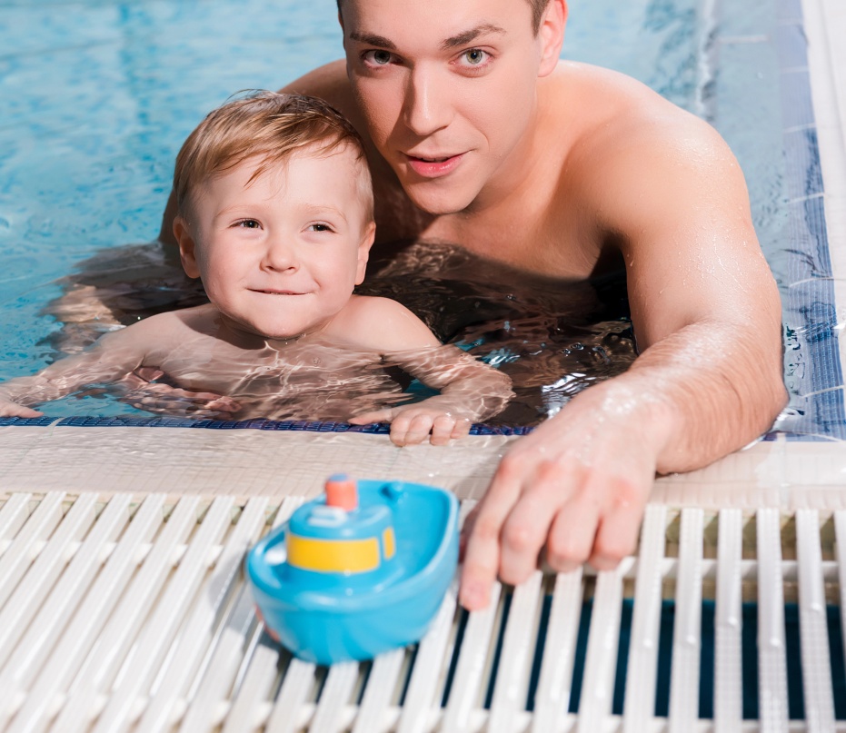 father and toddler son in pool with toy boat image
